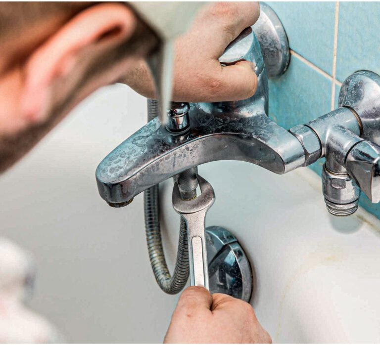Plombier serrant un flexible de baignoire avec une clé sur un robinet chromé encrassé.